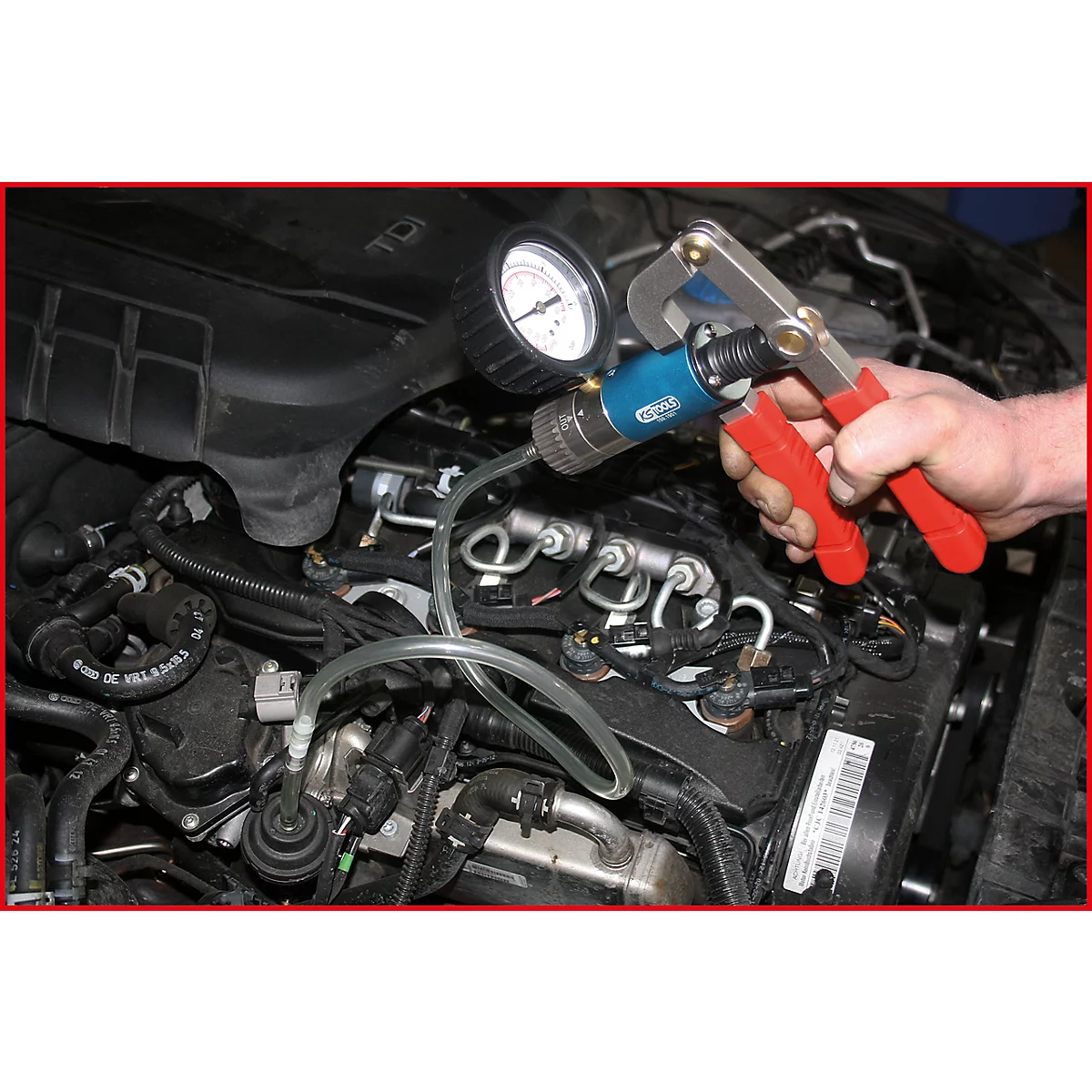 Ein Mechaniker überprüft ein Autoteil mit einem Messgerät. Die roten Griffe einer Zange umgreifen das blaue Messgerät.